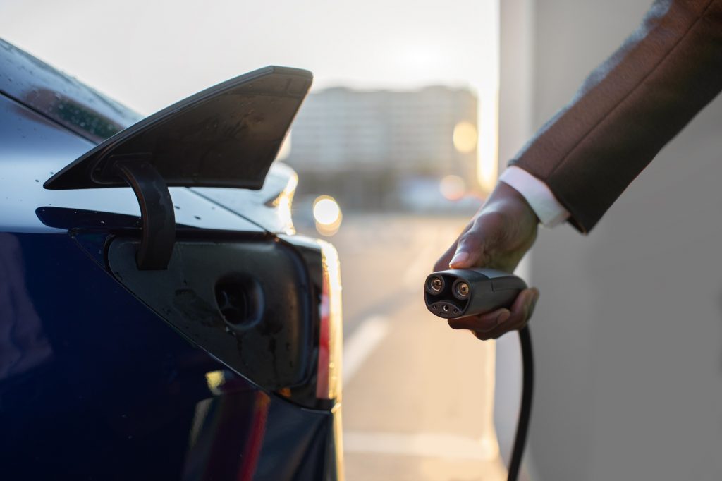 man's hand preparing to charge an electric car at outdoor charging station in the city