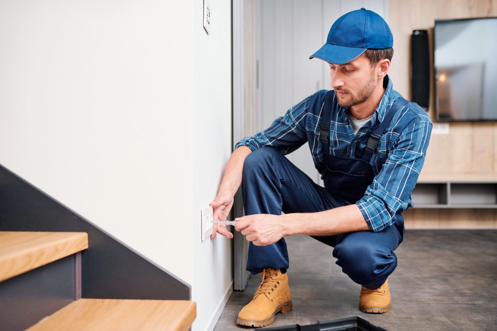Young electrician from household maintenance service checking voltage of socket